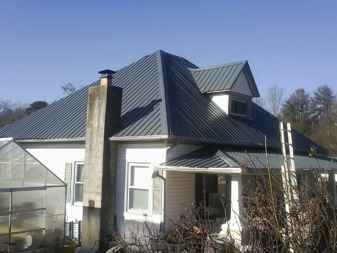 Dark blue standing seam metal roof on a white farmhouse with dormer — Slate & Tile Roof Repair by Roofing Brothers in Gardena