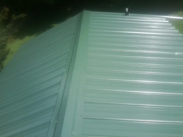 New green metal panels meeting at the ridge of a roof — Flat Roof Repair work by our crew in Gardena