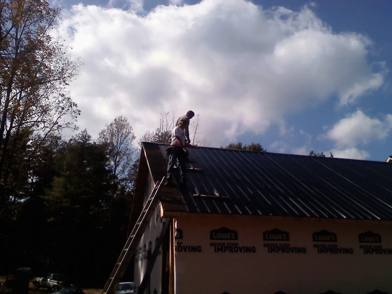 Roofer fastening dark metal panels high against a cloudy sky, from a Roof Inspection job in Gardena